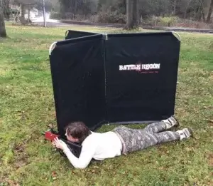 A person lying on the grass behind a laser tag barrier.