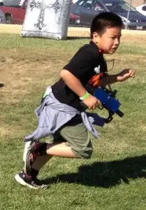 A young boy running with a laser tag tagger in his hands.