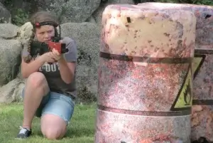 A girl kneeling down next to a barrel at a laser tag party.