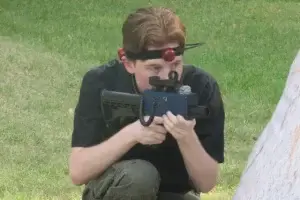 A young man crouching down with a laser tag tagger in his hands.
