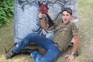 A young man sitting on the ground with a laser tag tagger.