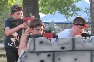A group of boys playing laser tag behind a barrier that looks like a brick wall.