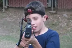 A young boy holding a laser tag tagger with a red light on it.