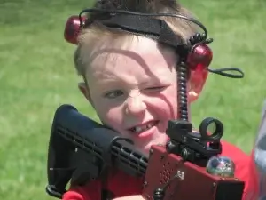 A young boy holding a laser tag tagger and wearing sensors on his head.