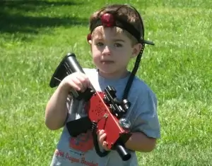 A young boy holding a laser tag tagger in the grass.