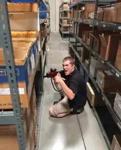 A man kneeling on the floor playing laser tag in a warehouse.